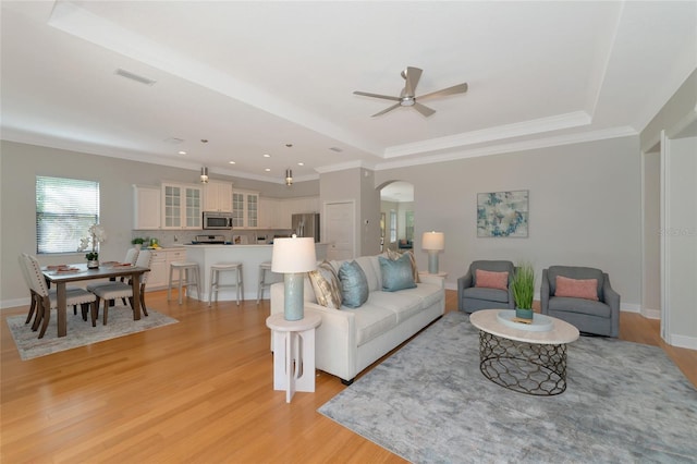 living room with a raised ceiling, ceiling fan, light hardwood / wood-style flooring, and crown molding