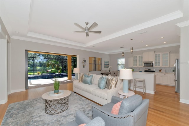 living room featuring ceiling fan, a raised ceiling, ornamental molding, and light hardwood / wood-style flooring