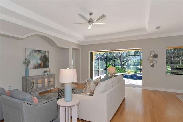 living room with ceiling fan, light hardwood / wood-style floors, a raised ceiling, and crown molding