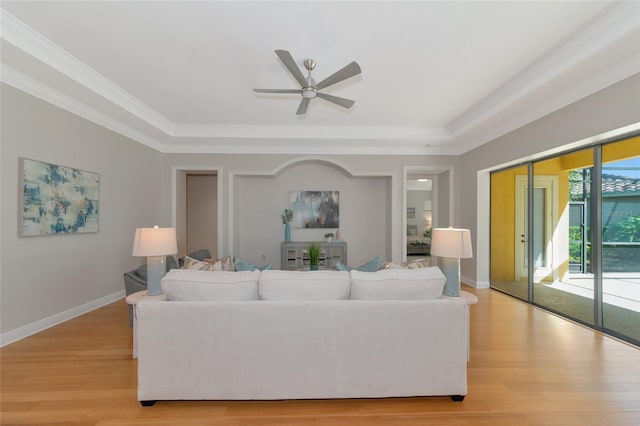 living room with a raised ceiling, light hardwood / wood-style flooring, ceiling fan, and crown molding