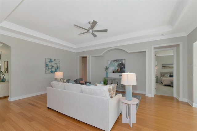 living room with light hardwood / wood-style floors, ceiling fan, crown molding, and a tray ceiling