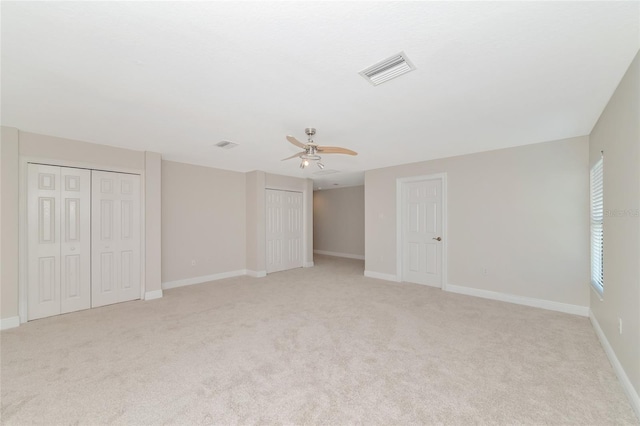 interior space featuring multiple closets, ceiling fan, and light carpet