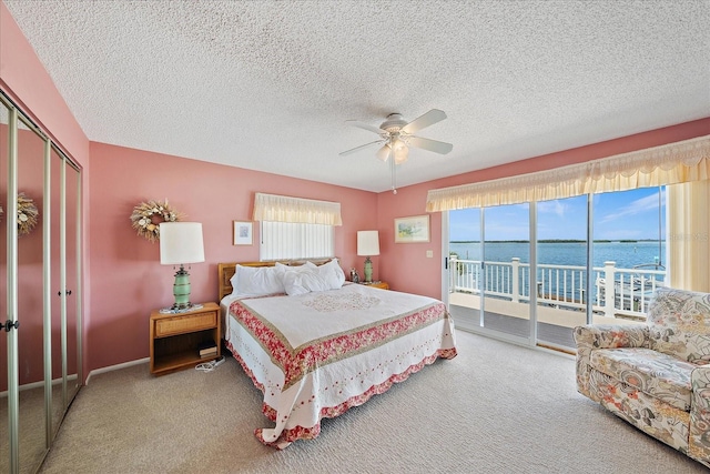 carpeted bedroom with a textured ceiling, access to outside, a water view, a closet, and ceiling fan