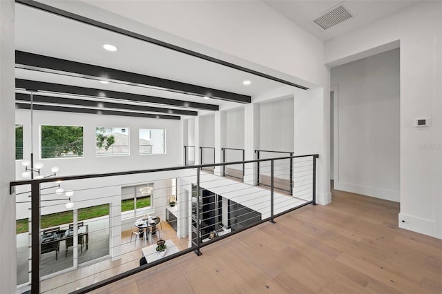 corridor with beamed ceiling, light hardwood / wood-style floors, and a notable chandelier