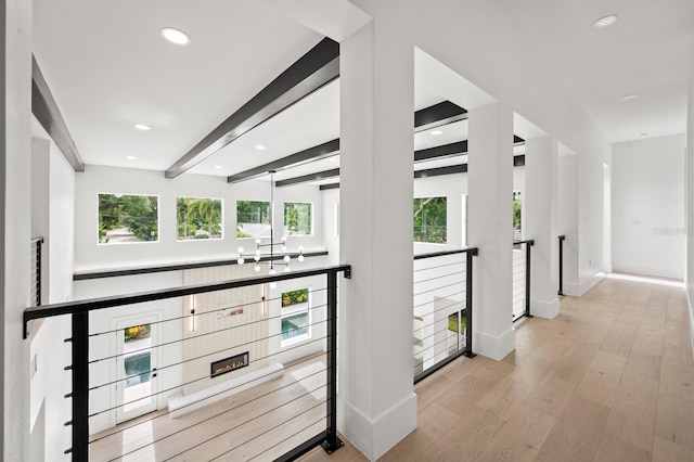 corridor with plenty of natural light, beam ceiling, and light hardwood / wood-style flooring