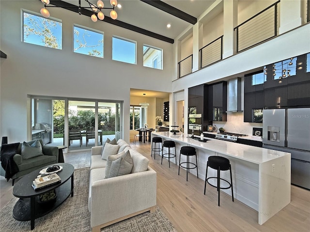 living room featuring sink, light wood-type flooring, a towering ceiling, beamed ceiling, and a notable chandelier