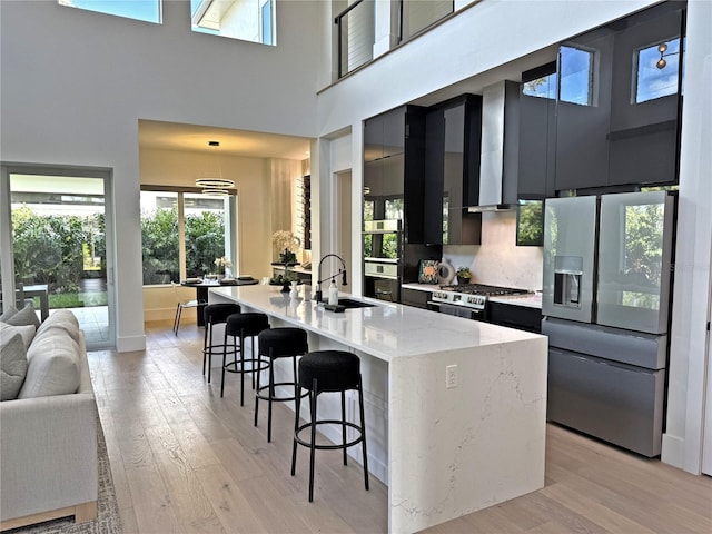 kitchen featuring appliances with stainless steel finishes, light wood-type flooring, a kitchen island with sink, pendant lighting, and a high ceiling