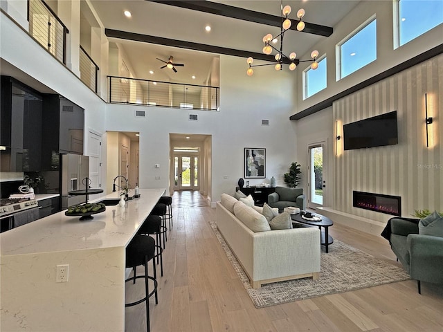 living room featuring beam ceiling, a towering ceiling, and light hardwood / wood-style flooring