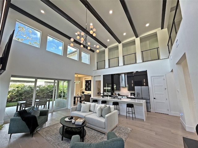 living room featuring beamed ceiling, light wood-type flooring, a high ceiling, and an inviting chandelier