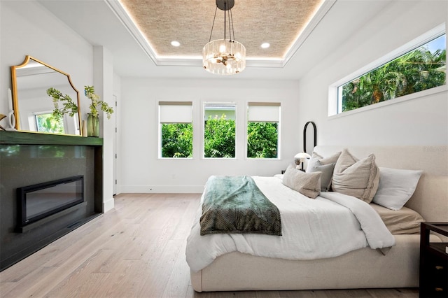 bedroom featuring a tray ceiling, a notable chandelier, and light wood-type flooring