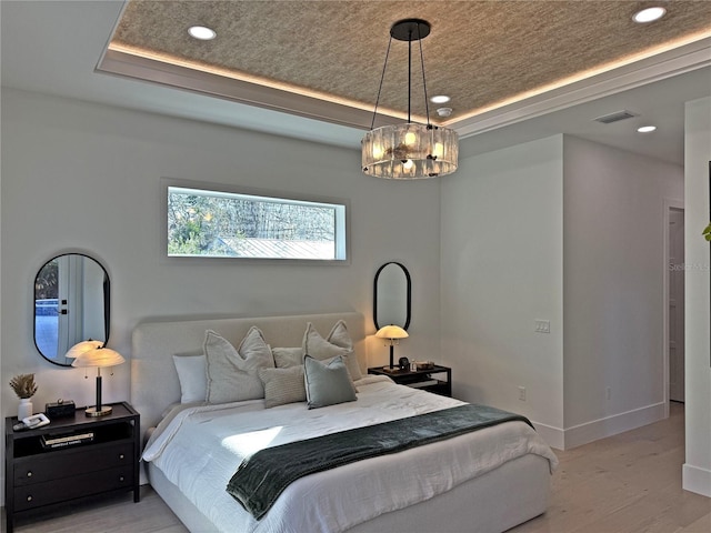 bedroom with light wood-type flooring and a tray ceiling