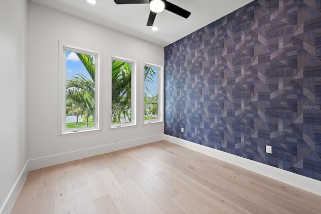 spare room featuring light hardwood / wood-style floors, ceiling fan, and tile walls