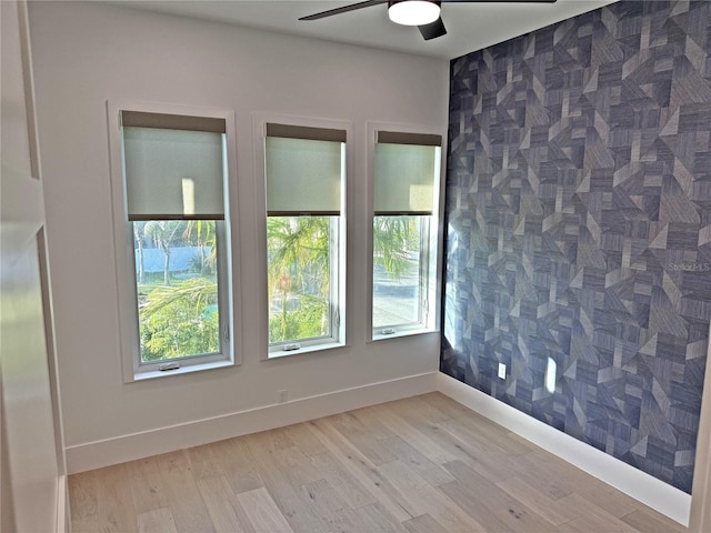 unfurnished room with light wood-type flooring, tile walls, and ceiling fan