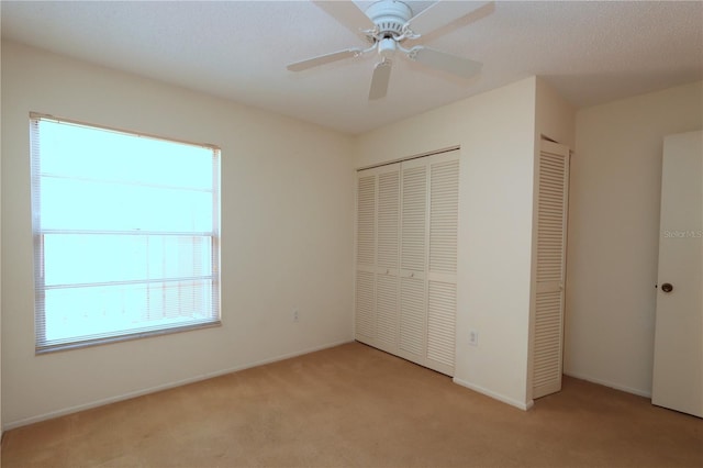 unfurnished bedroom featuring multiple windows, light colored carpet, ceiling fan, and multiple closets