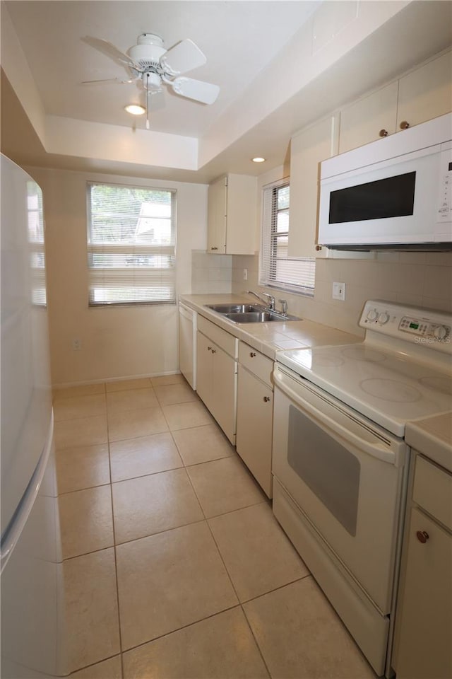 kitchen with sink, light tile patterned floors, white appliances, a tray ceiling, and white cabinets