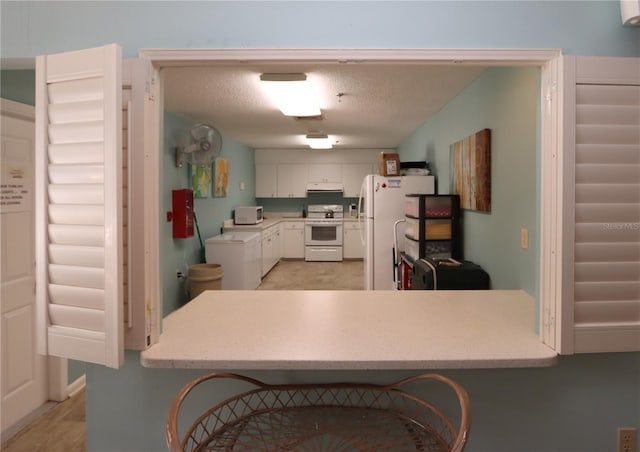 kitchen featuring a kitchen bar, kitchen peninsula, white cabinets, and white appliances