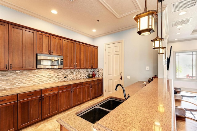 kitchen featuring pendant lighting, sink, light stone countertops, and crown molding