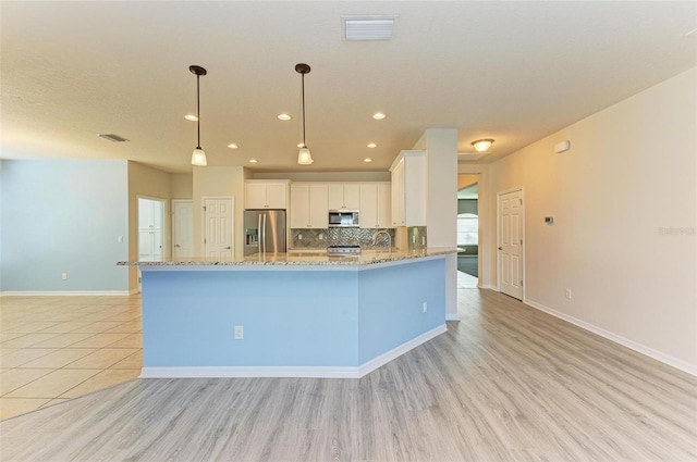 kitchen with pendant lighting, white cabinets, light wood-type flooring, tasteful backsplash, and stainless steel appliances