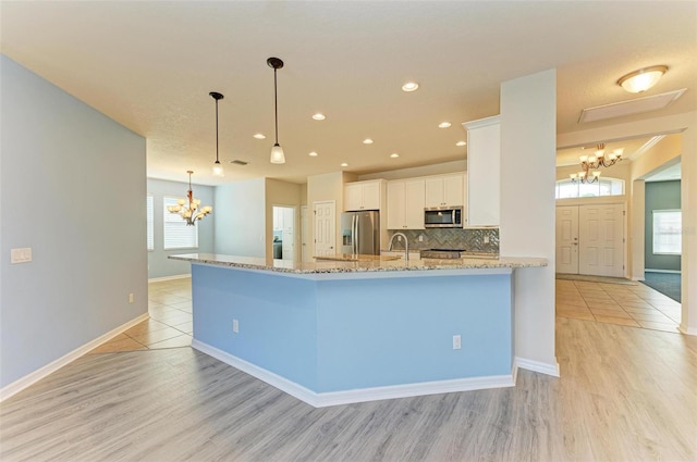 kitchen with appliances with stainless steel finishes, backsplash, light wood-type flooring, pendant lighting, and white cabinets