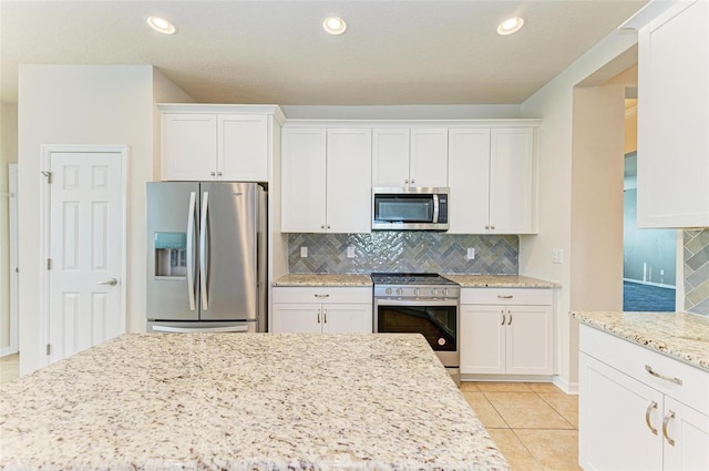 kitchen featuring light tile patterned flooring, white cabinetry, stainless steel appliances, light stone countertops, and tasteful backsplash