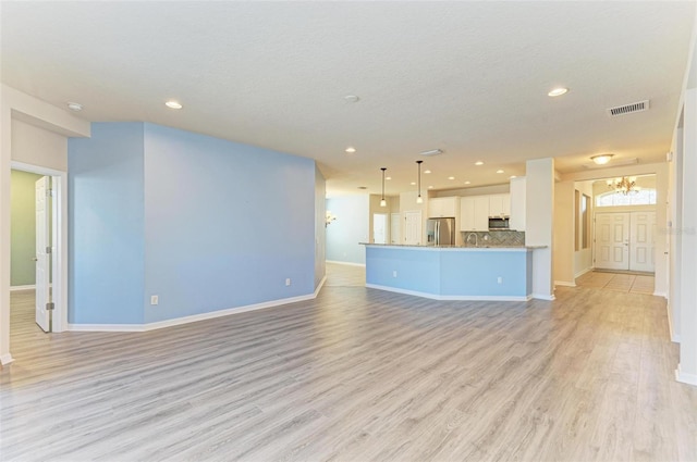 unfurnished living room featuring sink, light wood-type flooring, an inviting chandelier, and a textured ceiling