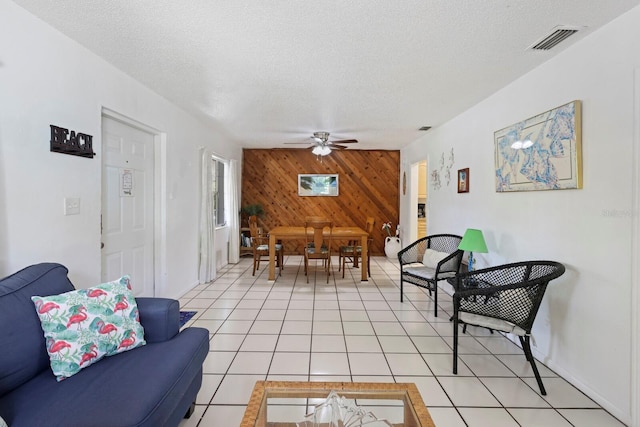 living room featuring wooden walls, ceiling fan, light tile patterned flooring, and a textured ceiling