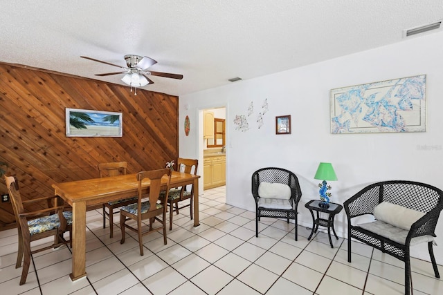 tiled dining area featuring ceiling fan, wood walls, and a textured ceiling