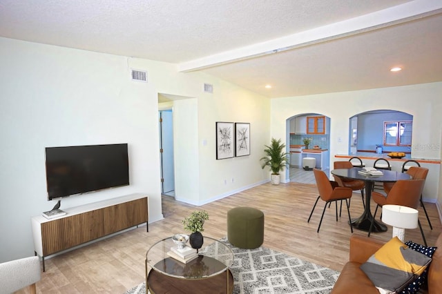 living room with lofted ceiling with beams, a textured ceiling, and light hardwood / wood-style flooring