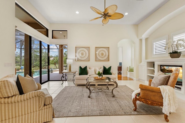 tiled living room featuring a high ceiling, a multi sided fireplace, a healthy amount of sunlight, and ceiling fan