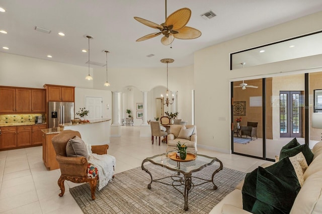 living room with light tile patterned floors, ceiling fan with notable chandelier, and ornate columns