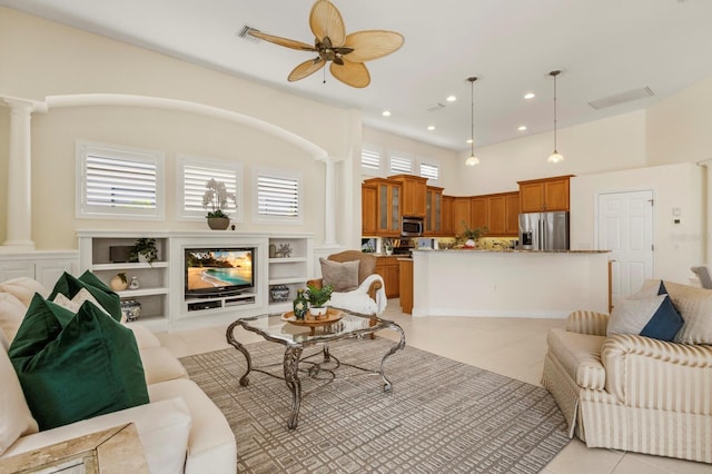 tiled living room featuring a towering ceiling, a fireplace, decorative columns, and ceiling fan