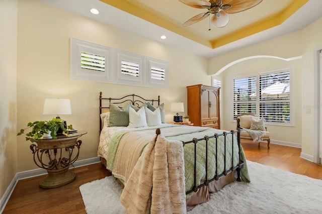 bedroom with ceiling fan, a tray ceiling, and hardwood / wood-style floors