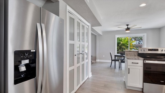 kitchen with white cabinets, stainless steel appliances, light stone counters, and ceiling fan