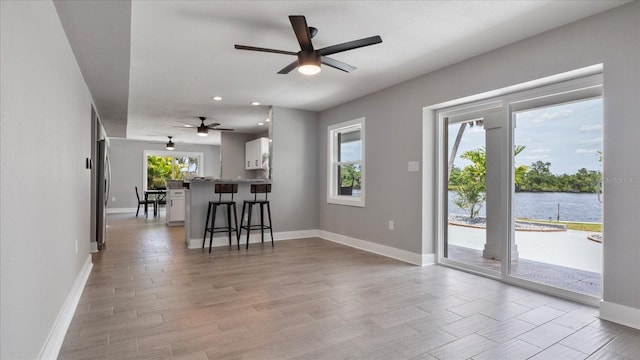 unfurnished living room featuring ceiling fan, plenty of natural light, and a water view