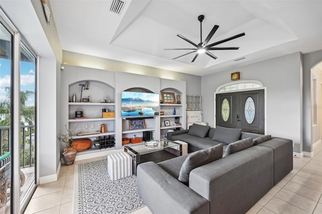 tiled living room featuring built in shelves, a raised ceiling, plenty of natural light, and ceiling fan