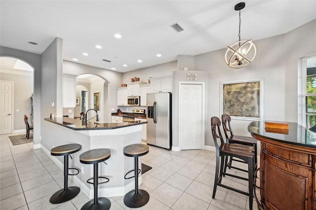 kitchen featuring kitchen peninsula, stainless steel appliances, decorative light fixtures, an inviting chandelier, and white cabinets