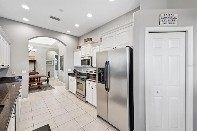 kitchen with dark stone counters, stainless steel appliances, a chandelier, white cabinetry, and light tile patterned flooring