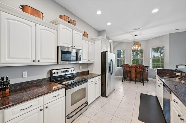 kitchen featuring stainless steel appliances, sink, light tile patterned floors, decorative light fixtures, and white cabinetry