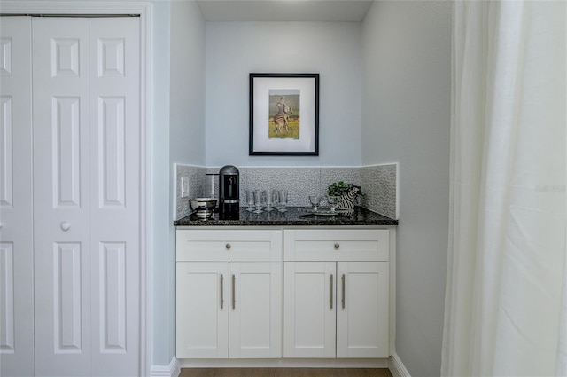 bar with white cabinets, dark stone countertops, and backsplash