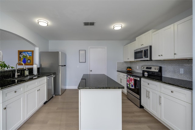 kitchen with dark stone counters, stainless steel appliances, sink, light hardwood / wood-style flooring, and white cabinets