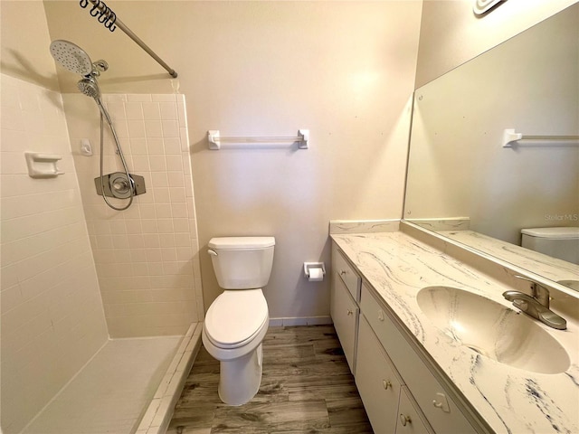 bathroom featuring hardwood / wood-style flooring, vanity, toilet, and a tile shower