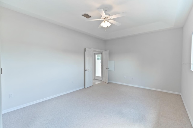 carpeted spare room with a tray ceiling and ceiling fan