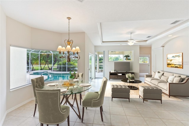 tiled dining room with plenty of natural light, ceiling fan with notable chandelier, and a tray ceiling