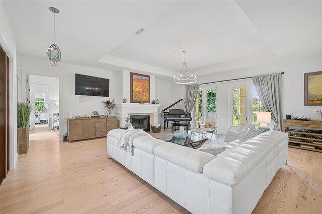 living room featuring a raised ceiling, a chandelier, and light wood-type flooring