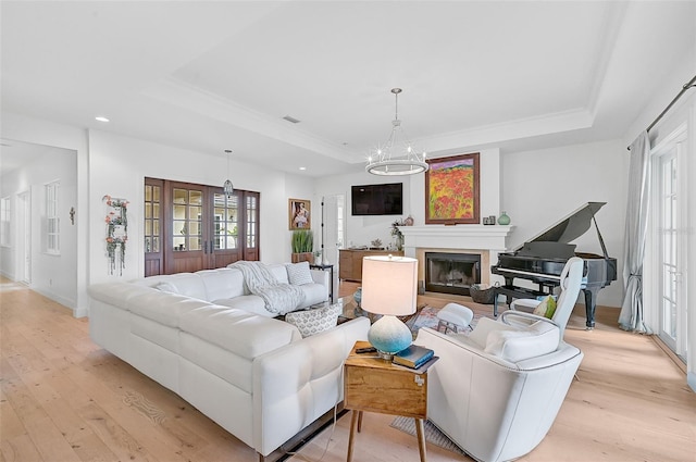 living room featuring a raised ceiling, light wood-type flooring, and an inviting chandelier