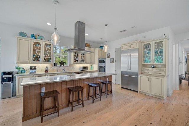 kitchen featuring built in appliances, a center island, island exhaust hood, and cream cabinets