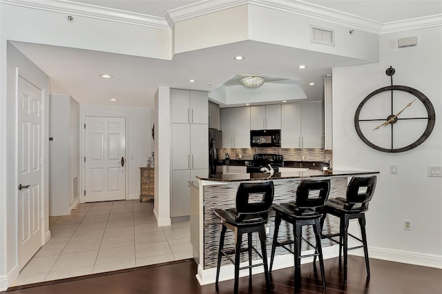 kitchen with kitchen peninsula, ornamental molding, a breakfast bar, black appliances, and white cabinetry