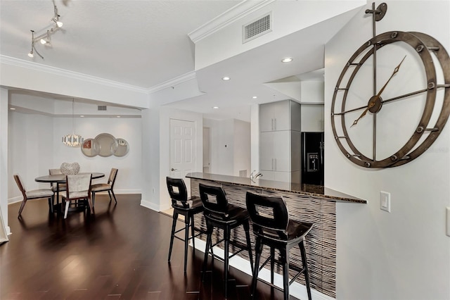 kitchen with dark stone countertops, crown molding, kitchen peninsula, and dark wood-type flooring