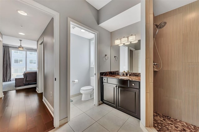 bathroom with ceiling fan, tiled shower, toilet, vanity, and hardwood / wood-style flooring