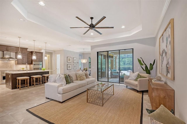 tiled living room with a raised ceiling, ceiling fan, sink, and ornamental molding